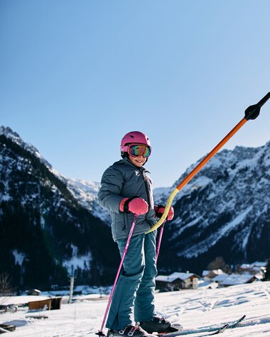 A child skiing in winter with snow-covered mountains and clear sky in the background | © Kleinwalsertal Tourismus eGen • Photographer: Oliver Farys