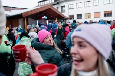 People celebrating outdoors at a winter event with music and shared joy, wearing winter clothing and hats. | © Kleinwalsertal Tourismus eGen • Photographer: Oliver Farys