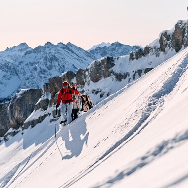 Zwei Schneeschuhwanderer klettern auf einer verschneiten Bergseite mit imposanten felsigen Gipfeln im Hintergrund im Kleinwalsertal. | © Kleinwalsertal Tourismus eGen • Fotograf: Oliver Farys