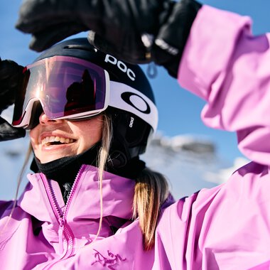 Young woman skiing in winter, wearing pink ski jacket, helmet, and goggles, smiling | © Kleinwalsertal Tourismus eGen • Photographer: Oliver Farys