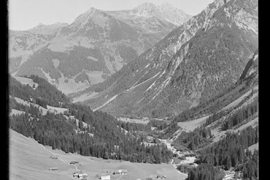 Schöne Berglandschaft im Tal mit kleinen Bauernhöfen, umgeben von hohen Gipfeln, im historischen Schwarz-Weiß-Foto. | © Kleinwalsertal Tourismus eGen • Karl Max Kessler Archiv