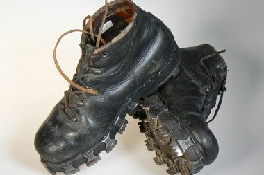 Old black mountaineering boots with worn soles, laces, and visible legs, black and brown. | © Kleinwalsertal Tourismus eGen • Stefan Heim