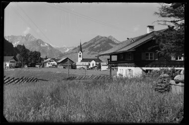 Historisches Bild von Riezlern mit Blick auf die Kirche und die umliegenden Berge, aufgenommen aus einer Wiese. | © Kleinwalsertal Tourismus eGen • Karl Max Kessler Archiv