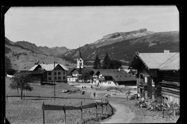 Historisches Foto von Riezlern, mit Kirchturm im Zentrum, umliegende Gebäude und Berge im Hintergrund. | © Kleinwalsertal Tourismus eGen • Karl Max Kessler Archiv