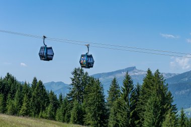 Two cabins of a cable car hang above a green forest landscape with mountains in the background on a sunny day. | © Oberstdorf · Kleinwalsertal Bergbahnen