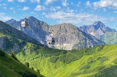 Summer Kanzelwand cable car with gondolas in the alpine landscape, green hills, mountains, and blue sky. | © Oberstdorf · Kleinwalsertal Bergbahnen