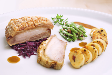 Crispy roasted pork with red cabbage, potato roulade, and green beans on a white plate. | © Kleinwalsertal Tourismus eGen • Photographer: Werner Krug