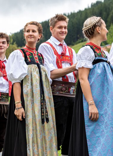 Gruppe von Menschen in traditionellen Trachten beim Alphornfestival im Grünen, mit Bergen im Hintergrund. | © Kleinwalsertal Tourismus eGen • Fotograf: Frank Drechsel