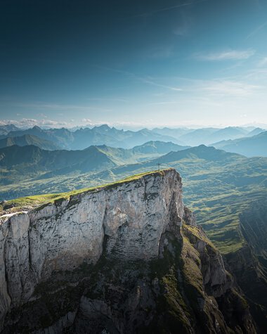 Berglandschaft mit grünen Hügeln und steilen Klippen unter einem blauen Himmel, aufgenommen vom Ifen. | © Kleinwalsertal Tourismus eGen • Fotograf: Robert Niederwolfsgruber