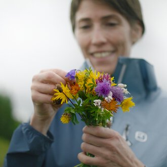 Woman picking a colorful bouquet of flowers outdoors, smiling. | © Kleinwalsertal Tourismus eGen • Photographer: Clemens Paul