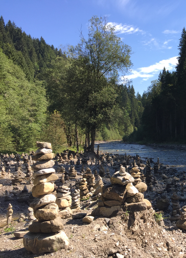 Wanderweg entlang eines Flusses in den österreichischen Alpen, umgeben von grünen Bäumen und Berglandschaft. | © Kleinwalsertal Tourismus eGen