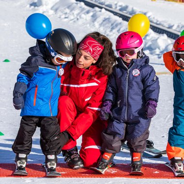 Children putting on ski boots in the snow, with a ski instructor on a winter sports area. | © Skischule Bödmen Baad