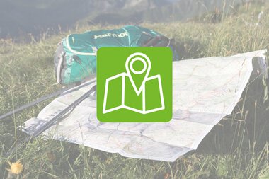 Eine Wanderkarte liegt auf grünem Gras, neben einer grünen Tasche, mit einer Markierung, die den Orientierungspunkt zeigt. | © Kleinwalsertal Tourismus eGen
