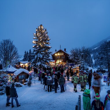 Festliche Winterveranstaltung am Adventszauber mit Besuchern, Weihnachtsbäumen und festlichem Lichterglanz in einer verschneiten Landschaft. | © Kleinwalsertal Tourismus eGen • Fotograf: Dominik Berchtold