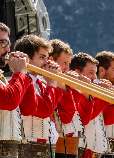 Fünf Männer in traditioneller Tracht spielen auf Alphörnern bei einem Fest im Freien. | © Kleinwalsertal Tourismus eGen • Fotograf: Frank Drechsel